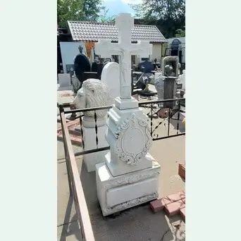 Памятник из белого мрамора с крестом. Обильно украшен резьбой.